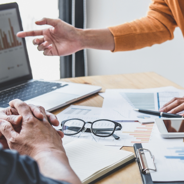 photo of two people working over a laptop with papers and eyeglasses on the table